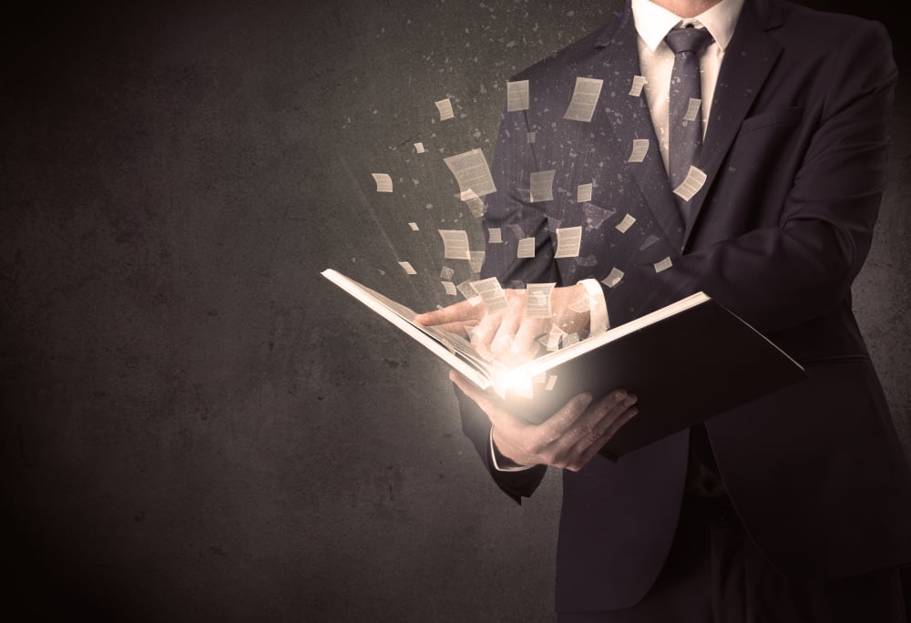 Man holding a book with document symbols around.